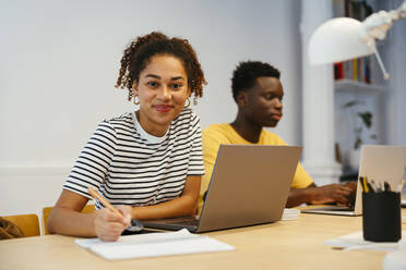 Lächelnder Student mit einem Freund, der einen Laptop im Hintergrund benutzt - EBSF03857