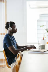 Student wearing wireless headphones studying on laptop at university - EBSF03875