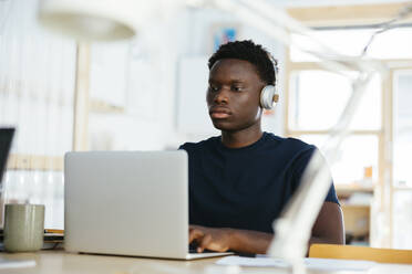 Junge Studentin mit kabellosen Kopfhörern und Laptop an der Universität - EBSF03881