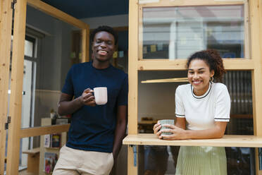 Happy young students standing with coffee cup in doorway at university - EBSF03907