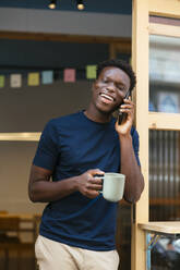 Happy student standing with coffee cup and talking on smart phone - EBSF03912