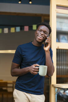 Glücklicher Student mit Kaffeetasse und Smartphone im Gespräch - EBSF03912