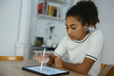 Student studying and writing on tablet PC at desk - EBSF03915