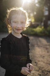 Smiling redhead girl standing in park - ANAF02185