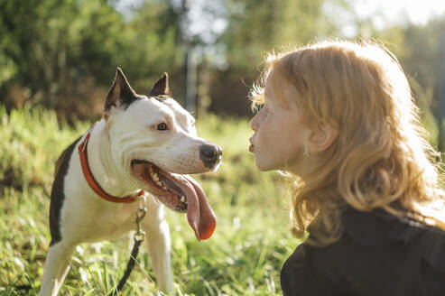 Rothaariges Mädchen bläst Hund im Park an einem sonnigen Tag einen Kuss zu - ANAF02190