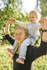 Smiling mother carrying daughter on shoulders in park - ANAF02194