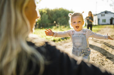 Happy daughter with arms outstretched running towards mother in park - ANAF02198