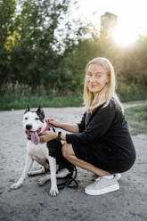 Smiling woman crouching near dog in park - ANAF02201