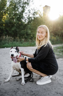 Lächelnde Frau hockt in der Nähe des Hundes im Park - ANAF02201