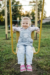 Smiling girl sitting on swing in park - ANAF02206