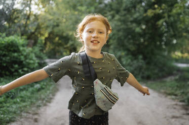 Happy redhead girl with arms outstretched in park - ANAF02212