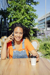 Lächelnder Student, der in einem Café mit seinem Smartphone telefoniert - PGF01677