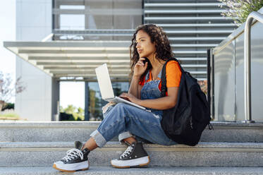 Nachdenklicher Student mit Laptop auf den Stufen des Campus sitzend - PGF01678