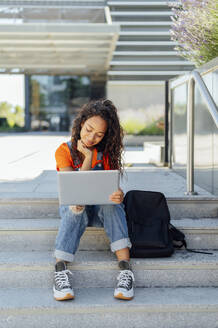 Lächelnder Student mit Rucksack und Laptop auf einer Treppe auf dem Campus - PGF01685