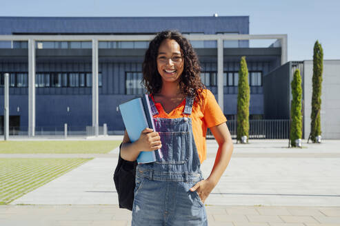 Lächelnder Student mit Hand in der Tasche auf dem Campus - PGF01693