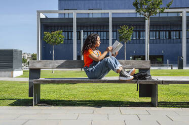 Young student sitting on bench and studying in front of building - PGF01705