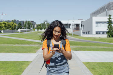Junge Studentin, die auf dem Campus spazieren geht und ein Mobiltelefon benutzt - PGF01706