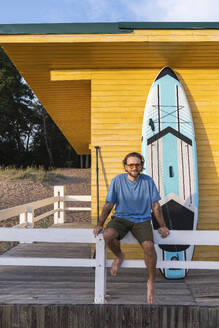 Junger Mann mit Paddleboard in der Nähe einer Strandhütte - VPIF08811