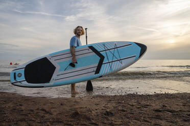 Young man carrying paddleboard at beach - VPIF08836