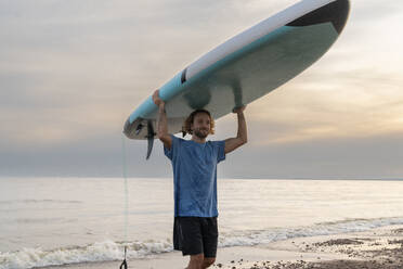 Lächelnder Mann mit Paddleboard in der Nähe von Meer unter Himmel - VPIF08853