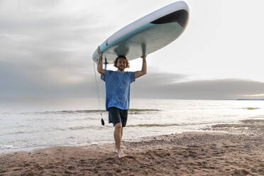 Lächelnder Mann mit Paddleboard und Spaziergang am Strand - VPIF08854