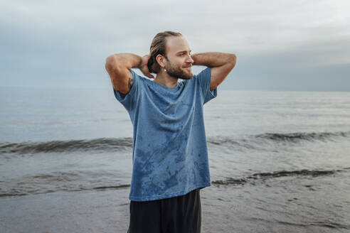 Smiling man with hands in hair standing at beach - VPIF08857