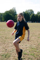Lächelndes Mädchen übt Fußball auf einem Sportplatz - AMWF01877