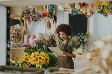 Lächelnder Jungunternehmer, der in einem Blumenladen in ein Klemmbrett schreibt - YTF01189