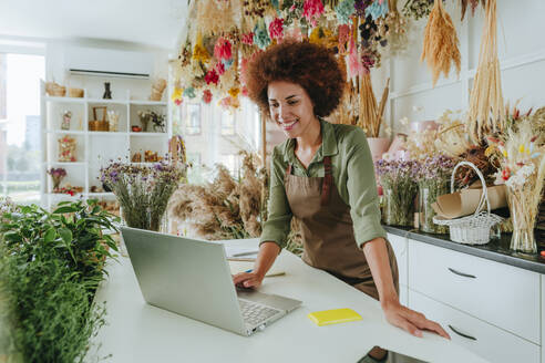 Lächelnder Afro-Ladenbesitzer mit Laptop am Schreibtisch im Blumenladen - YTF01210