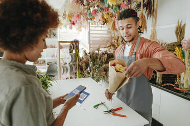 Customer paying through mobile phone by florist holding bouquet at flower shop - YTF01228