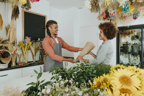 Lächelnder Florist, der einem Kunden im Blumenladen einen Blumenstrauß überreicht - YTF01230