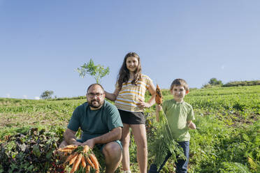 Father and children with carrots in field on sunny day - OSF02212