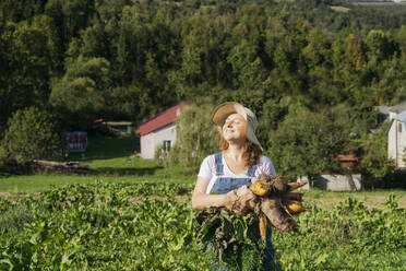 Frau mit Hut und Karotten in der Hand auf einem Feld an einem sonnigen Tag - OSF02215