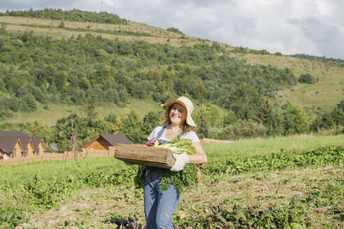 Lächelnde Frau mit Gemüsekiste im Feld stehend - OSF02220