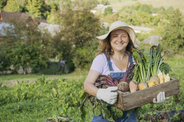 Smiling woman with root vegetables in crate at garden - OSF02222