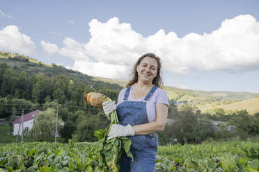 Smiling woman with fresh carrot standing in field - OSF02226