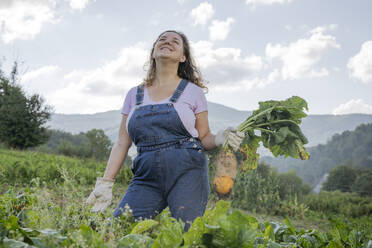 Woman with fresh carrot standing in field - OSF02227