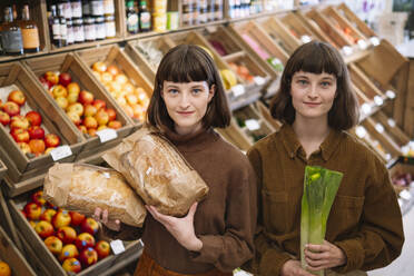Lächelnde Zwillingsschwestern in braunen Hemden mit Lebensmitteln auf dem Bauernmarkt - AMWF01888