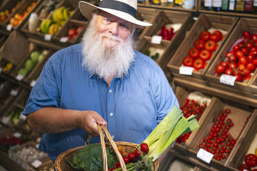 Senior man holding basket of vegetables at farmer's market - AMWF01896