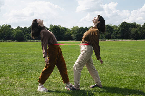 Happy twin sisters playing with plastic hoop at park - AMWF01899