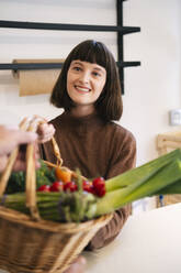 Lächelnde Frau mit Korb voller Gemüse im Laden - AMWF01909