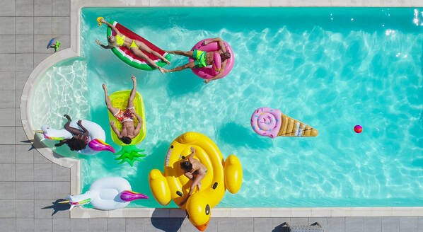 Happy people partying in an exclusive swimming pool with animal and fruit shapes mats, view from above - DMDF06921