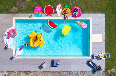 Happy people partying in an exclusive swimming pool with animal and fruit shapes mats, view from above - DMDF06923