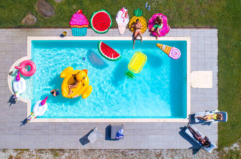Fröhliche Menschen beim Feiern in einem exklusiven Schwimmbad mit Matten in Form von Tieren und Früchten, Blick von oben - DMDF06923