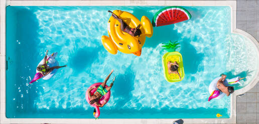 Happy people partying in an exclusive swimming pool with animal and fruit shapes mats, view from above - DMDF06925