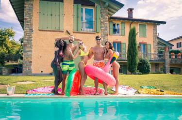 Multiracial group of friends having party in a private villa with swimming pool - Happy young people chilling with shaped air mattresses - DMDF06931