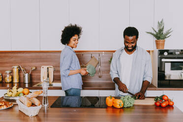 Schönes afroamerikanisches Paar, das zu Hause kocht - Schönes und fröhliches schwarzes Paar, das gemeinsam in der Küche das Abendessen vorbereitet - DMDF07129