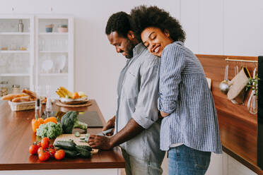 Schönes afroamerikanisches Paar, das zu Hause kocht - Schönes und fröhliches schwarzes Paar, das gemeinsam in der Küche das Abendessen vorbereitet - DMDF07131