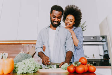 Schönes afroamerikanisches Paar, das zu Hause kocht - Schönes und fröhliches schwarzes Paar, das gemeinsam in der Küche das Abendessen vorbereitet - DMDF07132