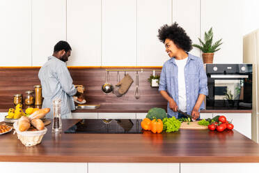 Beautiful afro american couple cooking at home - Beautiful and cheerful black couple preparing dinner together in the kitchen - DMDF07133